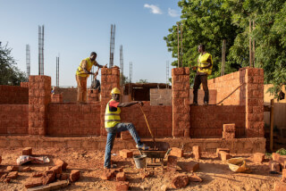 Three construction workers building a brick structure on a sunny day at a construction site.