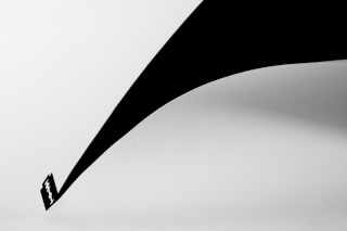 A minimalist black and white abstract studio shot featuring a razor blade and sharp cut against a stark white background.