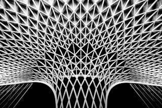 A low angle black and white shot of a geometric lattice structure creates a modern and abstract architectural view.