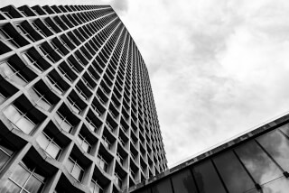 A striking black and white shot of a modern skyscraper against a cloudy sky, emphasizing architectural geometry.