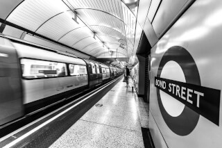 A train blurs by at the Bond Street tube station in London, captured in black and white.