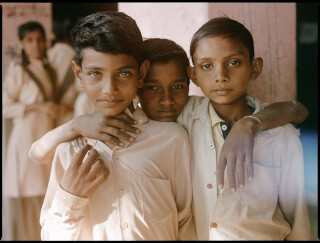 Three boys stand together, arms around each other, looking at the camera in a candid shot.