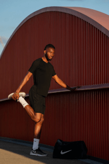 A sporty man in activewear stretches by a modern bridge with his gym bag, promoting a healthy and active lifestyle.