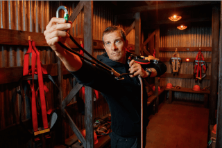 A man demonstrates climbing gear in an indoor facility with harnesses and safety equipment.
