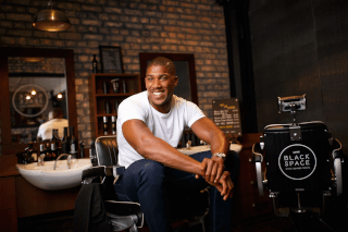 Anthony Joshua smiles, sitting in a stylish barbershop, for a grooming product promotion.