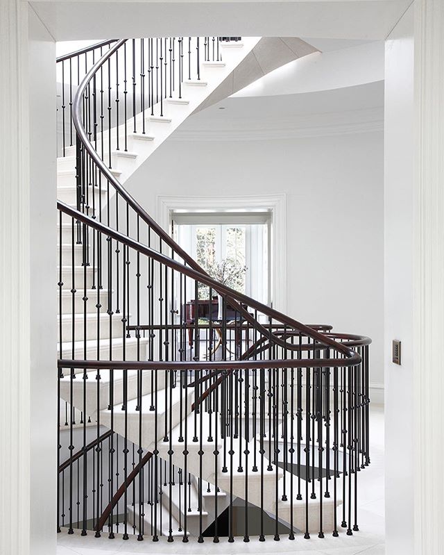 An elegant modern staircase with a dark wood handrail and white steps fills a light-filled hallway.