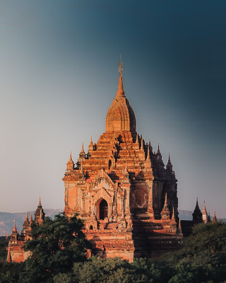 A beautiful buddhist temple in Bagan, Myanmar stands tall against a soft blue sky at sunset.