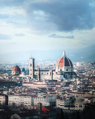 A scenic cityscape view of Florence, Italy, featuring the Duomo and surrounding architecture under a cloudy sky.