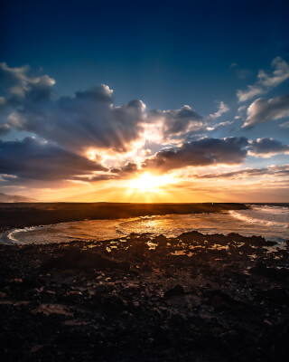 A breathtaking sunset over a rocky beach. The sun's rays illuminate the ocean and dark volcanic rocks.