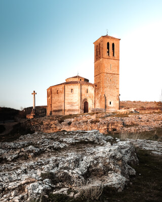 A historic church with a prominent tower stands on a rocky hilltop against a clear sky, showcasing classic architecture.