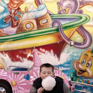 A young boy enjoys fluffy cotton candy at a colorful carnival, capturing a happy moment.