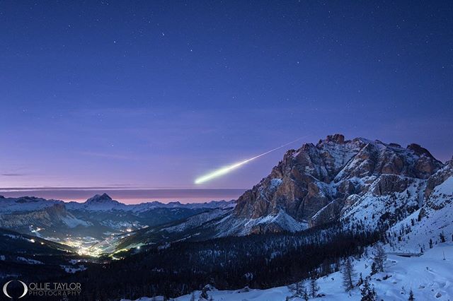 A stunning image of a meteor streaking across the night sky above snow-covered mountains and a village nestled in the valley.